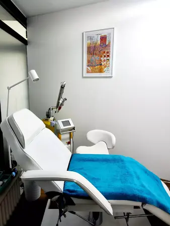 Moderner Behandlungsraum mit Liege, medizinischen Geräten und Wandbild zur Dermatologie.