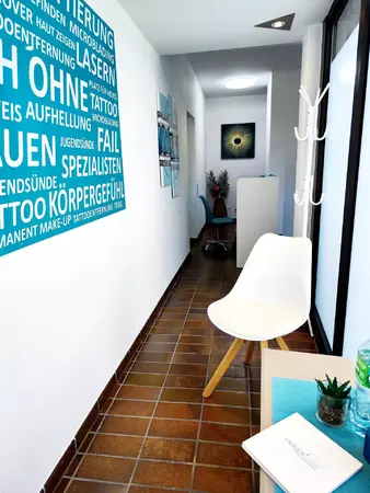 Moderner Wartebereich in einem Tattooentfernungsstudio mit Infotafel und Dekoration.