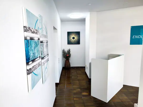 Heller Flur in einer Praxis mit moderner Kunst an weißen Wänden und Empfangstresen.